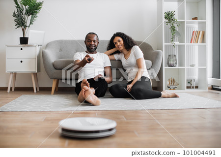 African man and woman using robot vacuum cleaner 101004491