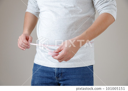 A man in a T-shirt and jeans is measuring his stomach size. Visceral fat reduction and diet image 101005151