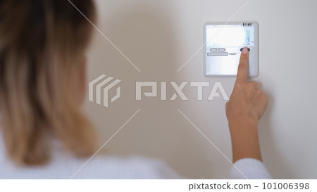 Woman pressing button on remote control of air conditioner in wall closeup 101006398