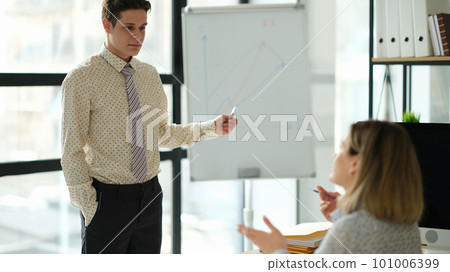 Business coach showing charts on blackboard to student in office 101006399