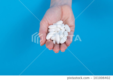 A woman is holding a handful of pills. A woman's hand sticks out of a hole in a cardboard blue background. 101006402