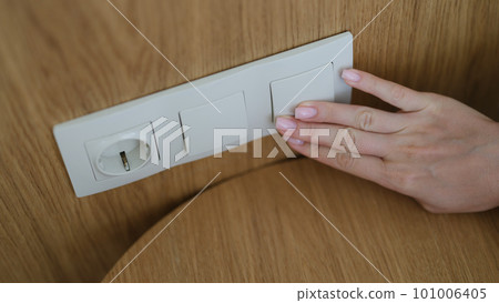 Hand pressing light switch in wall of house closeup 101006405