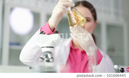 Scientist chemist looking at flask with yellow brake oil in chemistry lab closeup Scientist chemist looking at flask with yellow brake oil in chemistry lab closeup 101006445