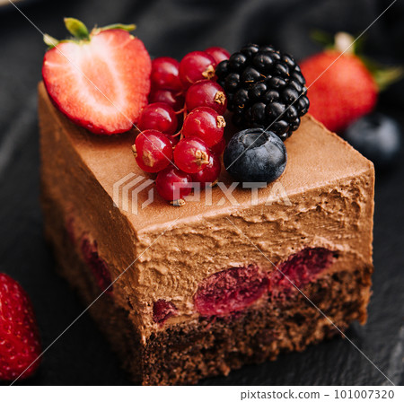 Delicious chocolate cake decorated with fresh berries on wooden black table Delicious chocolate cake decorated with fresh berries on wooden black table 101007320