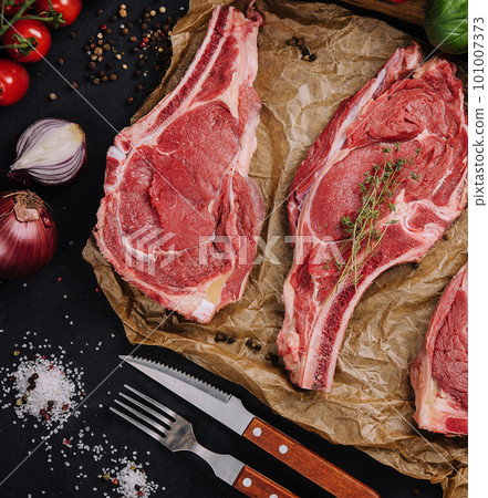 Three raw beef steaks on a wooden chopping board, garlic and a sprig of rosemary 101007373