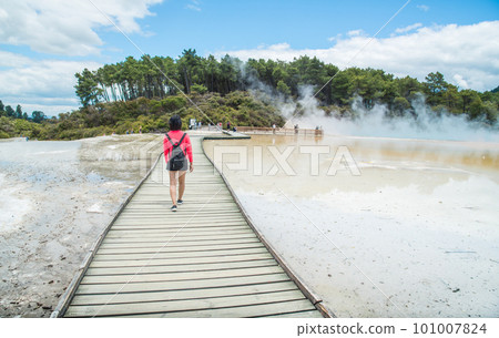 Asian tourist walking on the boardwalk across the Artist's Palette to Champagne pool an iconic tourist attraction of Wai-O-Tapu the geothermal wonderland in Rotorua, New Zealand. 101007824