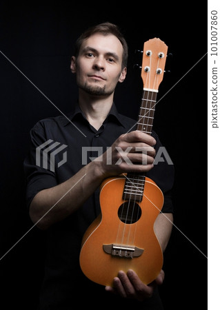 Handsome young low key man portrait with ukulele guitar over black background Handsome young low key man portrait with ukulele guitar over black background 101007860