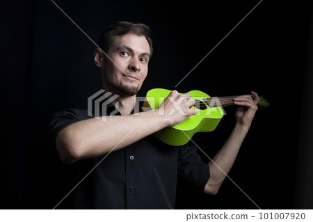 Handsome young low key man portrait with fun green ukulele guitar over black background Handsome young low key man portrait with fun green ukulele guitar over black background 101007920