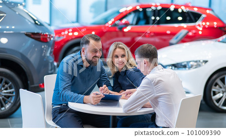 Happy caucasian couple signs a contract for the purchase of a car salon. Happy caucasian couple signs a contract for the purchase of a car salon. 101009390