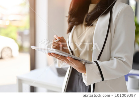 Cropped image of a confident Asian businesswoman using her tablet while standing in the office Cropped image of a confident Asian businesswoman using her tablet while standing in the office 101009397
