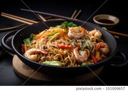 Stir fried noodles with shrimps and vegetables in cast iron cooking pan on dark table background Stir fried noodles with shrimps and vegetables in cast iron cooking pan on dark table background 101009657