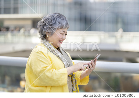 操作智能手機的 60 多歲女性 操作智能手機的 60 多歲女性 101009803
