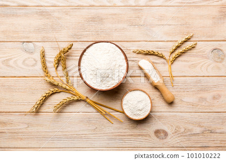 Flat lay of Wheat flour in wooden bowl with wheat spikelets on colored background. world wheat crisis Flat lay of Wheat flour in wooden bowl with wheat spikelets on colored background. world wheat crisis 101010222