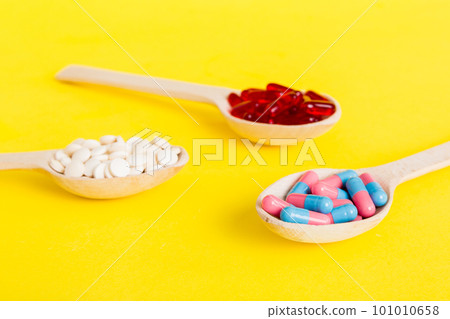 Vitamin capsules in a spoon on a colored background. Pills served as a healthy meal. Red soft gel vitamin supplement capsules on spoon 101010658