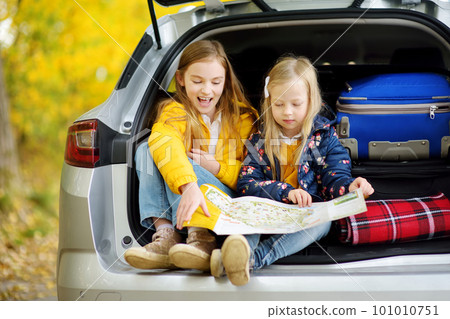 Two adorable girls sitting in a car trunk before going on vacations with their parents. Two kids looking forward for a road trip or travel. 101010751
