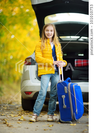 Adorable girl with a suitcase ready to go on vacations with her parents. Child looking forward for a road trip or travel. Autumn break at school. 101010753