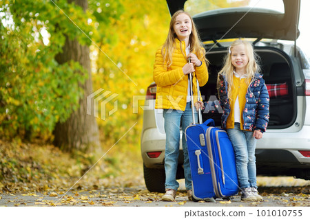 Two adorable girls with a suitcase going on vacations with their parents. Two kids looking forward for a road trip or travel. Autumn break at school. 101010755