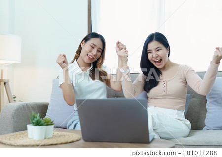 lgbtq, lgbt concept, homosexuality, portrait of two asian women posing happy together and loving each other while playing computer laptop on sofa. lgbtq, lgbt concept, homosexuality, portrait of two asian women posing happy together and loving each other while playing computer laptop on sofa. 101011288