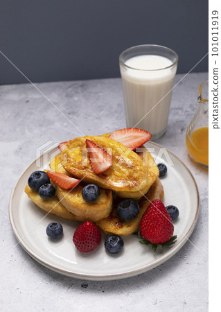Torrijas, French Toast Made Of Sliced Brioche, Bread, Served With Orange Syrup, Fresh Blueberries, Strawberry On Plate, Glass Of Milk on Granite Table. Dessert for breakfast. Vertical plane 101011919