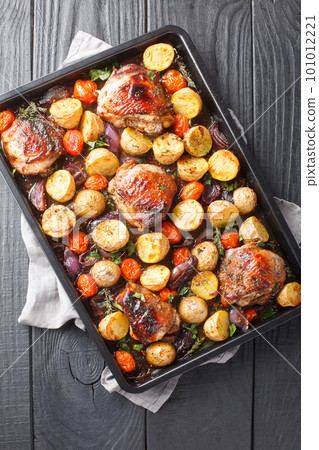Balsamic chicken with potatoes, red onion and tomatoes close-up on a baking sheet. Vertical top view 101012221