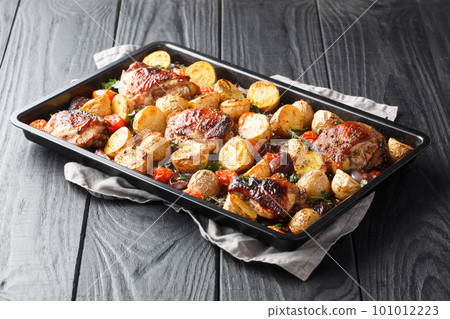 Chicken thighs baked with potatoes, garlic, onions and tomatoes close-up on a black baking sheet. horizontal Chicken thighs baked with potatoes, garlic, onions and tomatoes close-up on a black baking sheet. horizontal 101012223