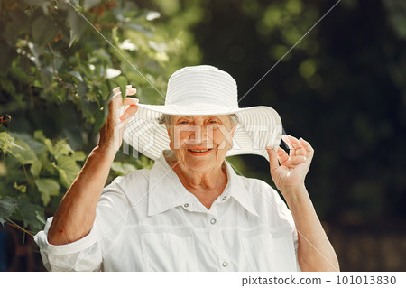 Portrait of beautiful aged woman in the park. Grandma in a white hat. 101013830