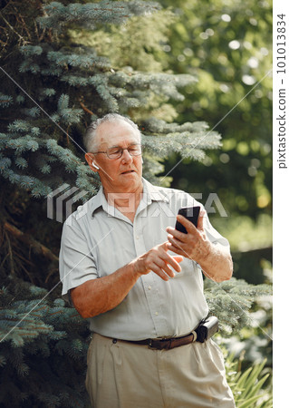 Technology, people and communication concept. Senior man at summer park. Grangfather using a phone. Technology, people and communication concept. Senior man at summer park. Grangfather using a phone. 101013834