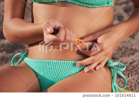 A young woman injects herself with insulin on the beach in summer. Active recreation for diabetes. 101014811