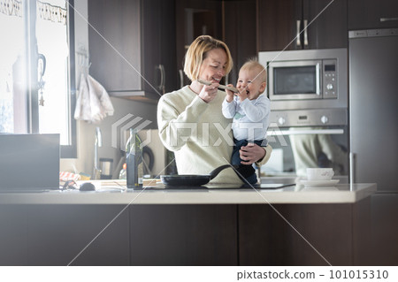 Happy mother and little infant baby boy cooking and tasting healthy dinner in domestic kitchen. Family, lifestyle, domestic life, food, healthy eating and people concept 101015310