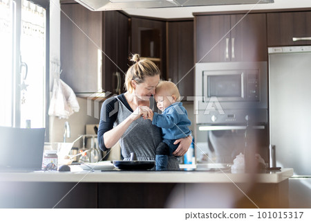 Happy mother and little infant baby boy making pancakes for breakfast together in domestic kitchen. Family, lifestyle, domestic life, food, healthy eating and people concept 101015317