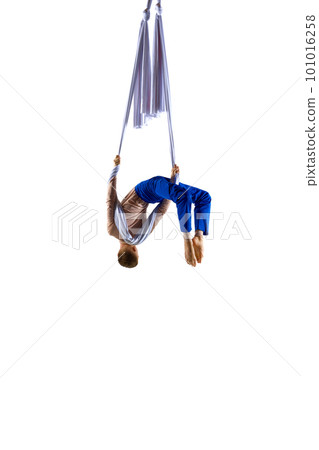 Dynamic image of young man, professional, flexible aerial gymnast doing acrobatic tricks with aerial ribbon against white studio background 101016258