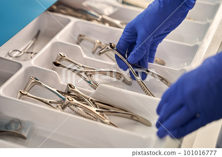 Doctor's hands wearing a disposable medical gloves holding a stainless steel nasal speculum for ENT examination over other surgery instruments Doctor's hands wearing a disposable medical gloves holding a stainless steel nasal speculum for ENT examination over other surgery instruments 101016777