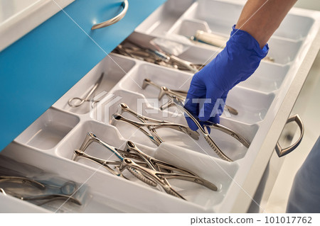 Doctor's hands wearing a disposable medical gloves holding a stainless steel nasal speculum for ENT examination over other surgery instruments 101017762