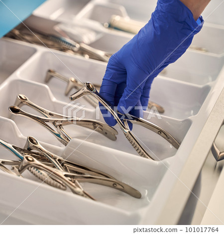Doctor's hands wearing a disposable medical gloves holding a stainless steel nasal speculum for ENT examination over other surgery instruments 101017764