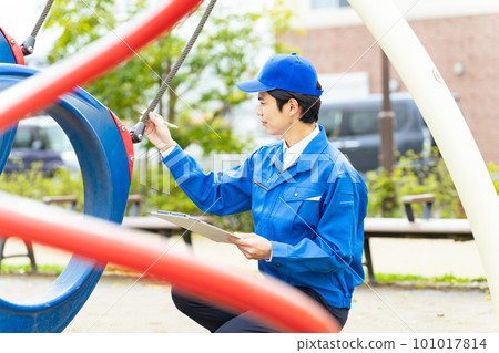 A male worker who inspects the playground equipment in the park for safety 101017814