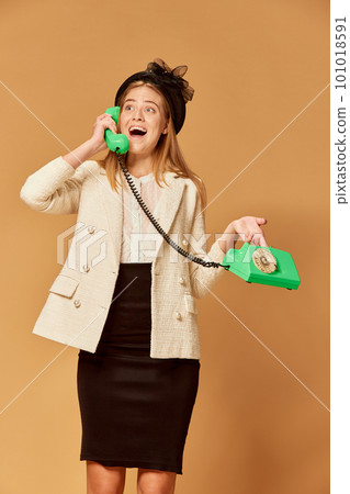 Pretty woman wearing old-fashioned clothes holding phone and talking with surprised face over orange background Pretty woman wearing old-fashioned clothes holding phone and talking with surprised face over orange background 101018591