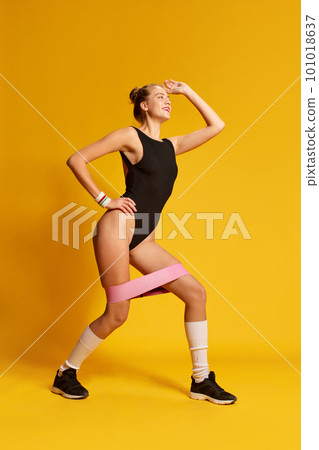 Portrait of sporty girl wearing swimsuit and doing exercise with rubber bands for sport over yellow background 101018637