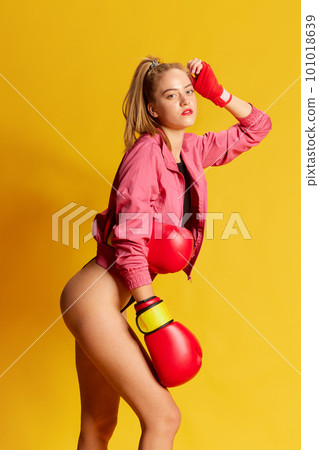 Sports girl wearing bodysuit and boxing gloves looking at camera with calm facial expression over yellow background Sports girl wearing bodysuit and boxing gloves looking at camera with calm facial expression over yellow background 101018639