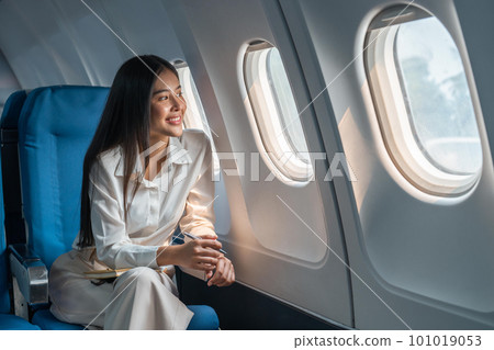 Asian woman sitting in a seat in airplane and looking out the window going on a trip vacation travel concept 101019053