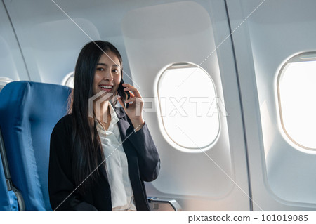 Successful young business woman working speaking on mobile phone while while sitting on aircraft cabinin 101019085