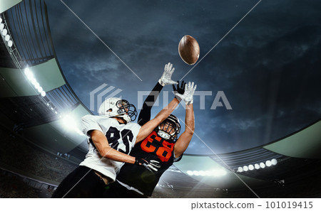 Dynamic shot of male sportsmen, professional american football players during game, catching ball. Open air 3D stadium in evening 101019415
