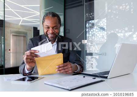 African american businessman reading good news, man inside office workplace holding mail envelope letter with good news, boss in business suit mature and adult. African american businessman reading good news, man inside office workplace holding mail envelope letter with good news, boss in business suit mature and adult. 101019685