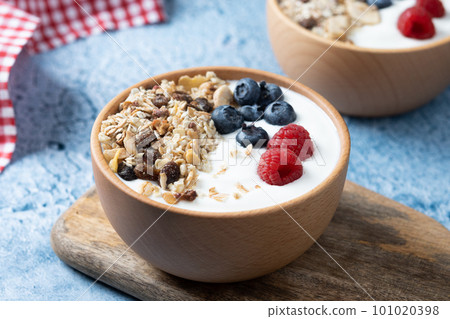 Yogurt with berries and muesli for breakfast in bowl on blue background 101020398