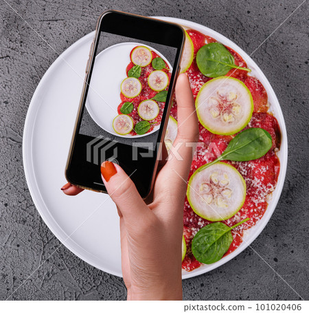 Female hand making a photo of Italian beef carpaccio with sliced zucchini Female hand making a photo of Italian beef carpaccio with sliced zucchini 101020406