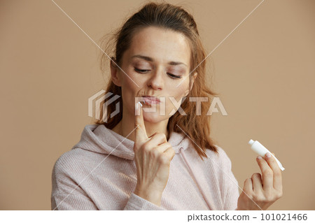 woman applying ointment using finger against beige background 101021466