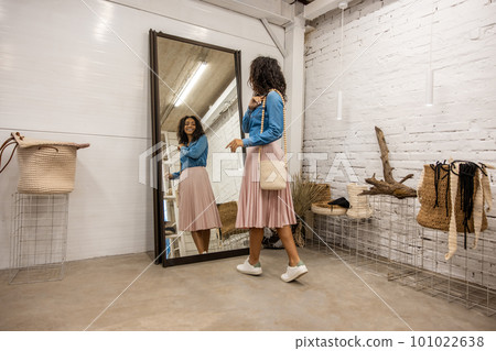 Cute young woman dressed in boho style posing near the mirror 101022638