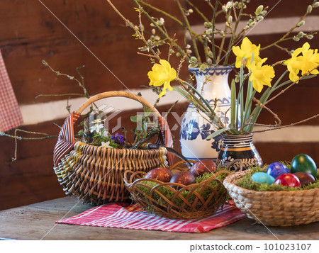 Easter and spring still life with wicker baskets, coloured decorated easter eggs ,moss, feather, vases flowers with narcissus on rustic wooden table in log cabin. Happy Easter holiday card Easter and spring still life with wicker baskets, coloured decorated easter eggs ,moss, feather, vases flowers with narcissus on rustic wooden table in log cabin. Happy Easter holiday card 101023107