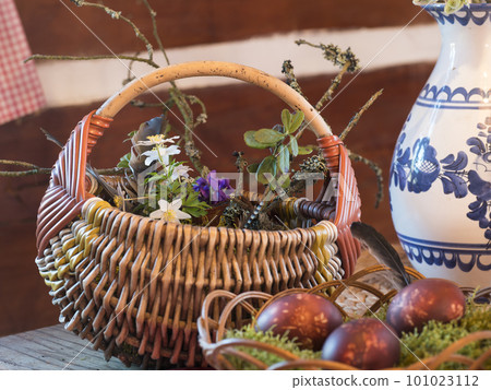 Two wicker baskets with brown onion coloured easter eggs decorated plant imprints, moss, feather, wood anemone and violet flowers in rustic log cabin. Happy Easter holiday card and spring still life Two wicker baskets with brown onion coloured easter eggs decorated plant imprints, moss, feather, wood anemone and violet flowers in rustic log cabin. Happy Easter holiday card and spring still life 101023112