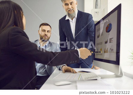 Woman showing some graphs and charts on the computer screen to her male colleagues 101023222