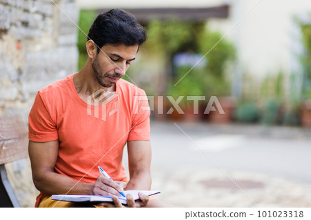 Indian mid adult south asian handsome man write outdoor on travel diary in Asturias, Spain  101023318